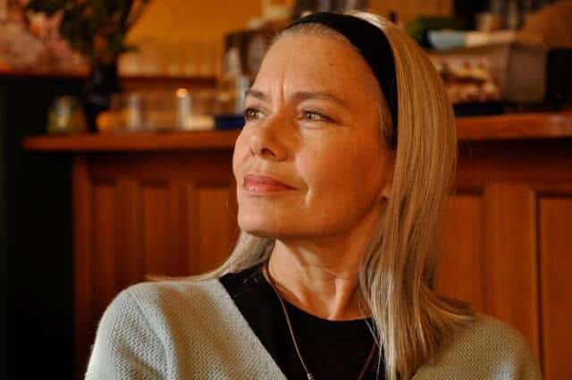 Candida Royalle, pelo rubio y diadema negra, pensativa y sonriente en un café